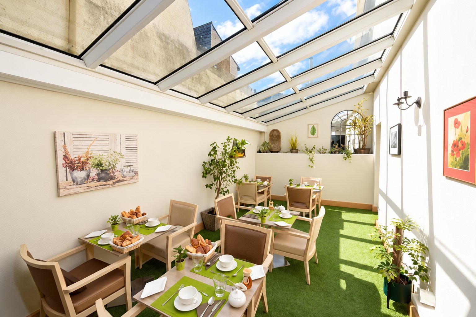 Une salle à manger sous verrière avec des tables dressées de sets verts, des chaises en bois, des plantes et un sol en gazon synthétique.