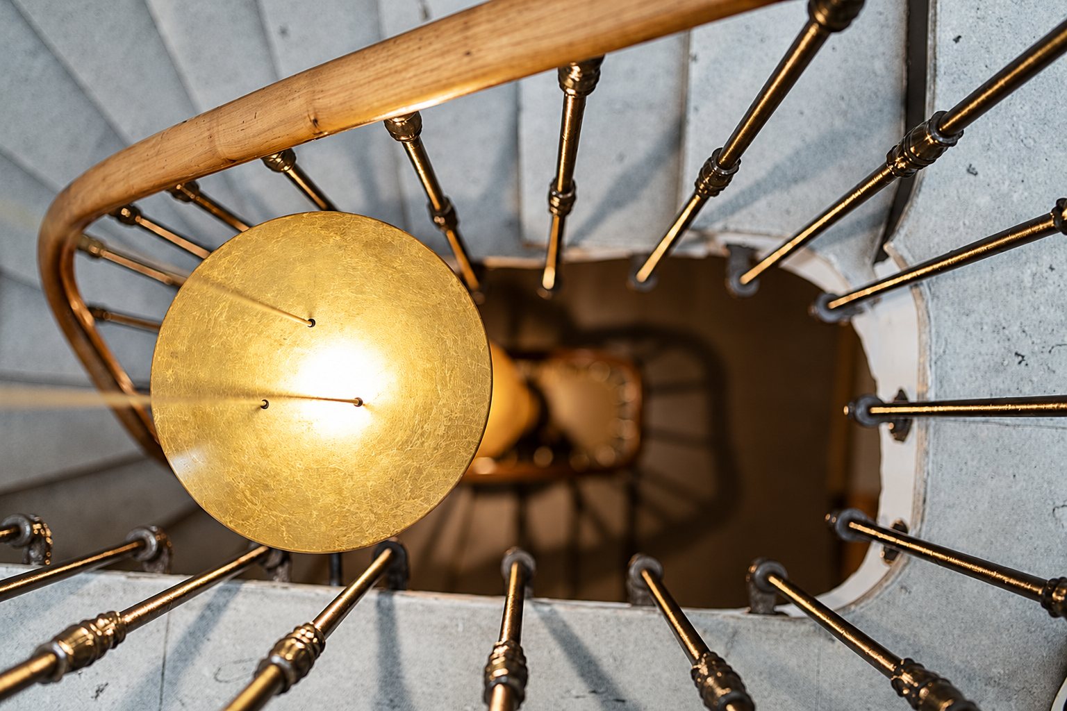 Vue du dessus d'un escalier en colimaçon aux balustres en laiton, avec une suspension circulaire à la feuille d'or éclairée au premier plan.